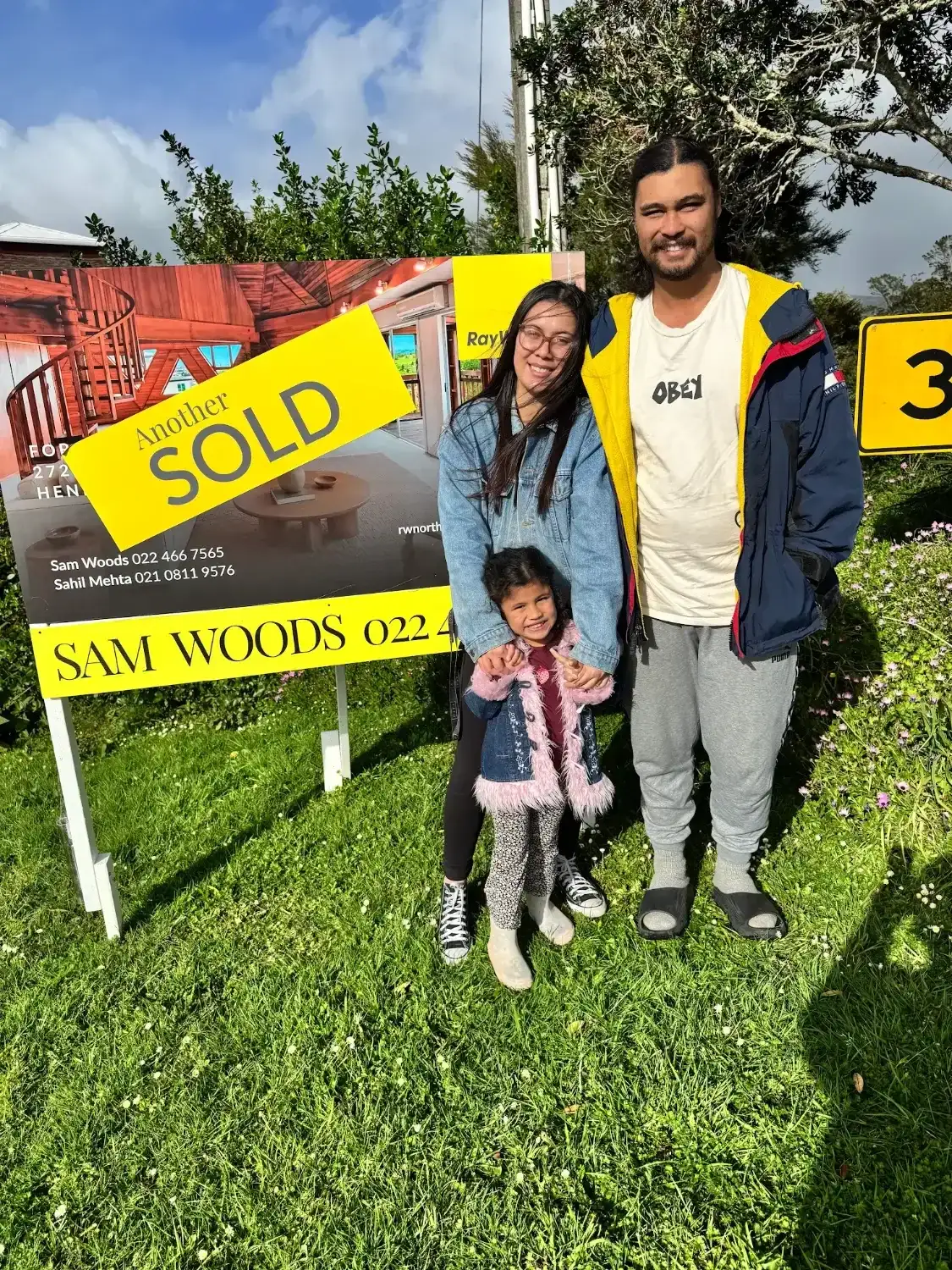Family of three beside their Sold sign