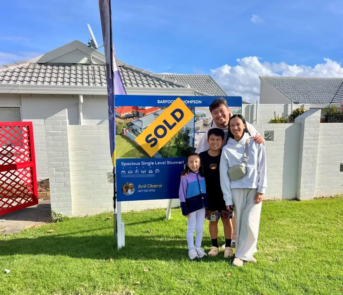 Family of four in front of their Sold sign