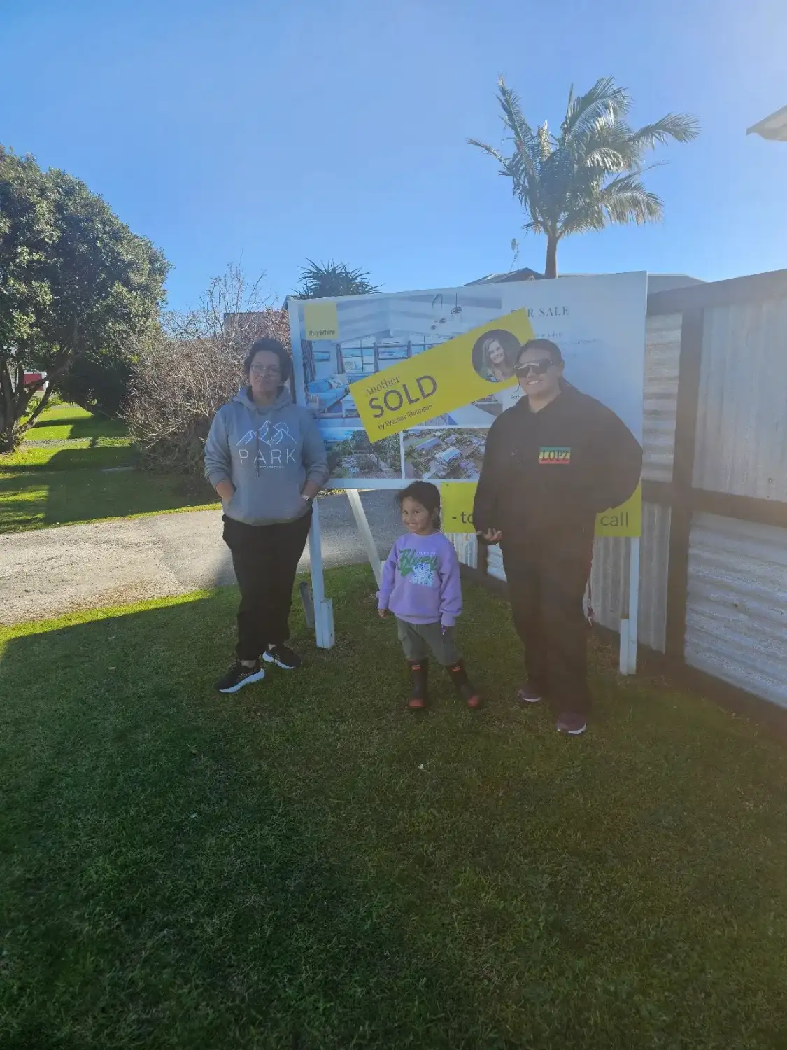 Family beside their Sold sign