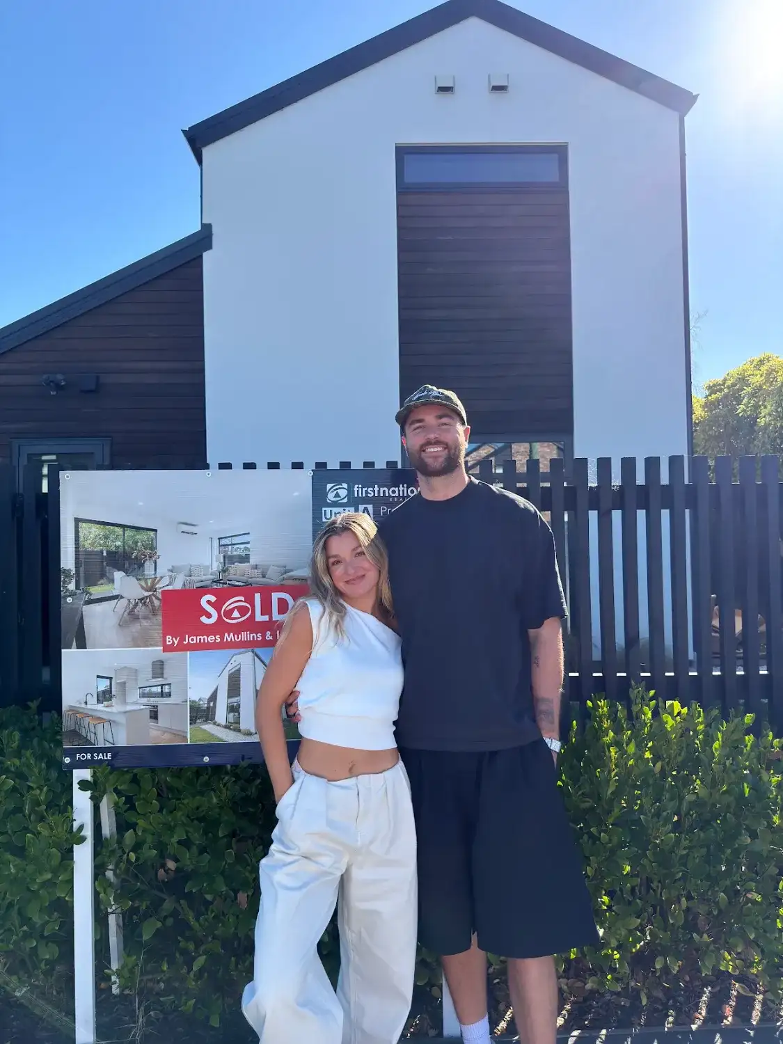 Couple in front of their new home with a Sold sign