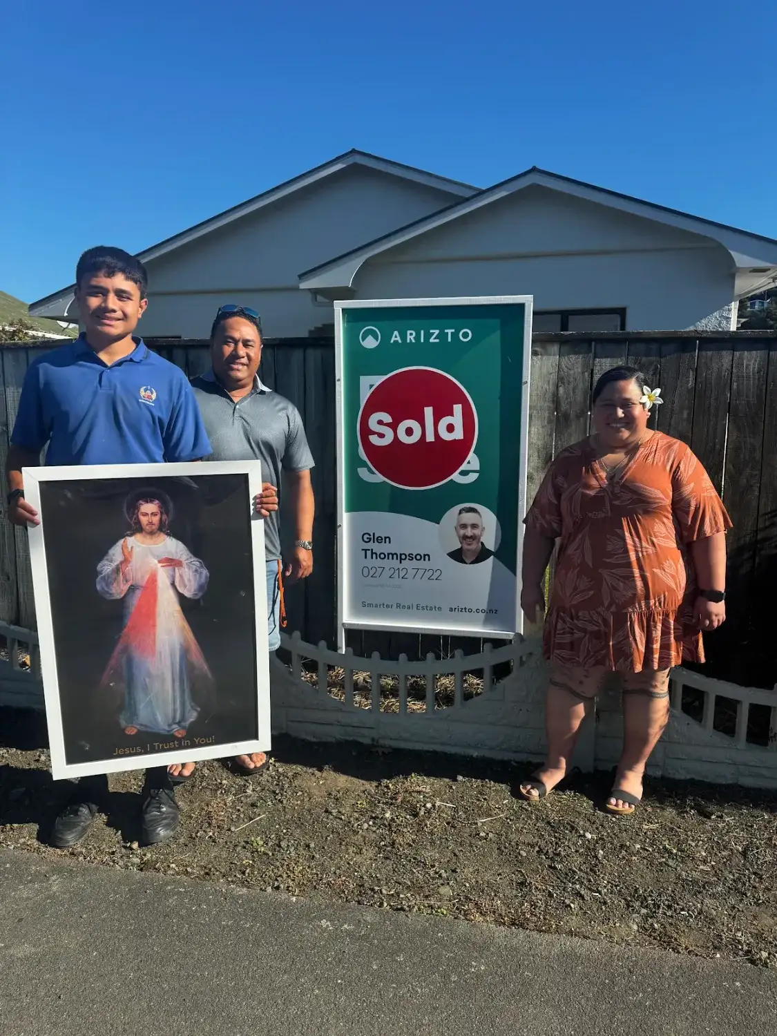 Family holding a picture beside their Sold sign