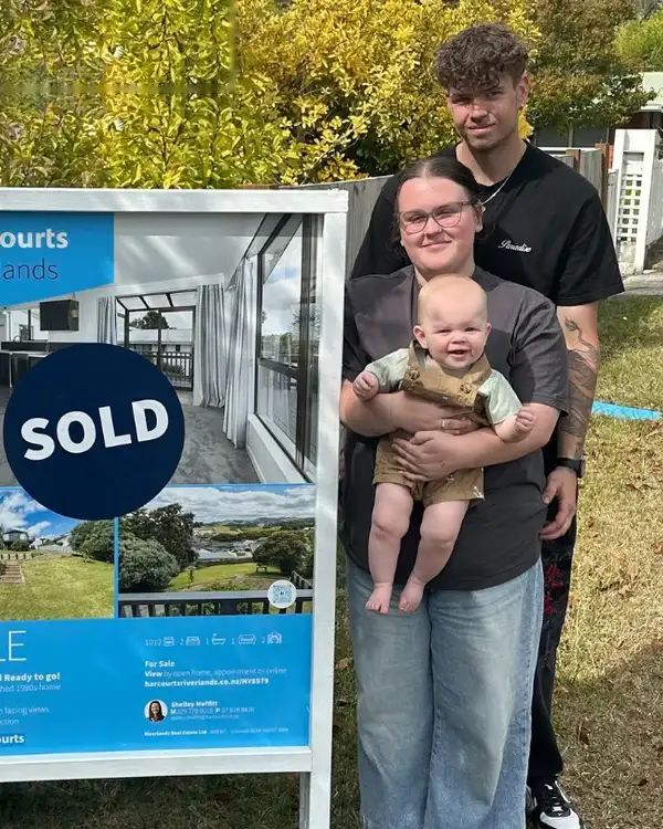 Young family with their baby beside their Sold sign