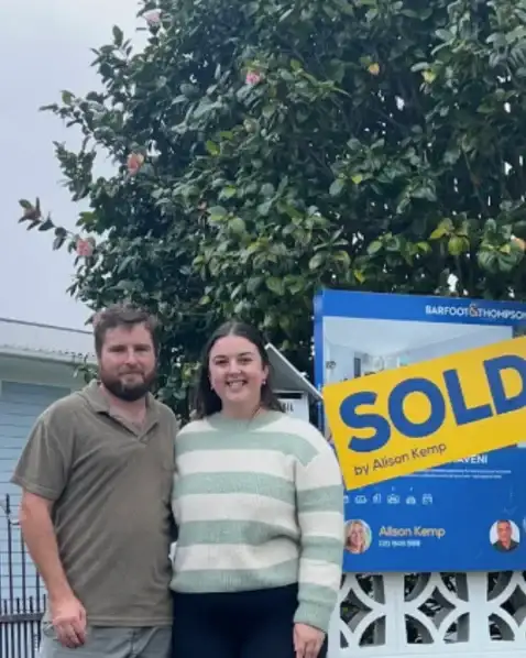 Couple outside their new home with a Sold sign