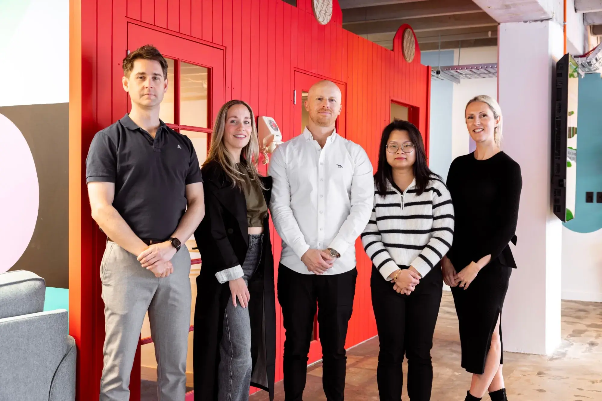 The Mortgage Man team standing together in front of a red wall